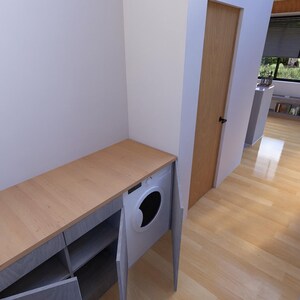 Puede incluir: Un lavadero con una encimera de madera clara y un armario gris con estantes abiertos. Una lavadora blanca est&aacute; integrada en el armario. La habitaci&oacute;n tiene suelo de madera clara y una puerta marr&oacute;n claro.