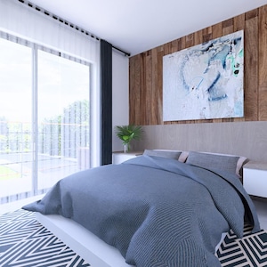 May include: A modern bedroom with a large bed covered in a blue comforter. The room features a wooden accent wall, a large window with dark curtains, and a geometric patterned rug. A piece of abstract art hangs above the bed.