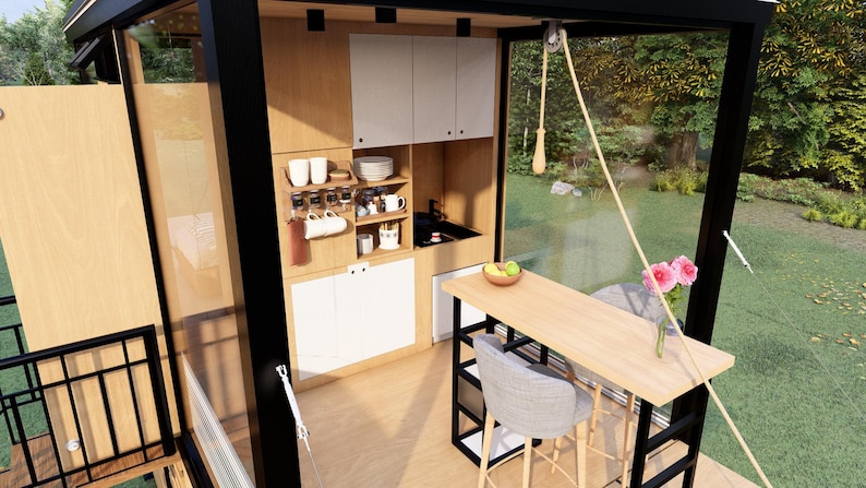 Pu&ograve; includere: Interno di una piccola casa moderna con cucina e zona pranzo. La cucina &egrave; dotata di mobili in legno chiaro, piani di lavoro bianchi e un piccolo lavandino. Un bancone in legno con due sgabelli e un vaso di fiori rosa si trova nella zona pranzo.