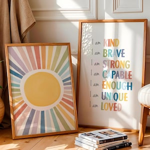 May include: Two framed art prints. One features a yellow sunburst design with rainbow rays. The other print has the words "I am KIND, BRAVE, STRONG, CAPABLE, ENOUGH, UNIQUE, LOVED" in colorful text. The frames are wood.