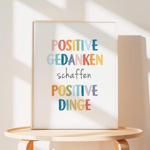 Peut inclure: Une impression encadr&eacute;e color&eacute;e avec le texte "POSITIVE GEDANKEN schaffen POSITIVE DINGE" dans un sch&eacute;ma de couleurs arc-en-ciel.