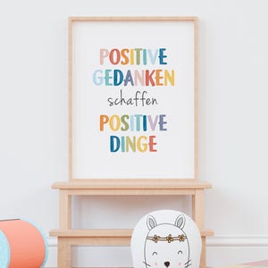 Peut inclure: Une impression encadr&eacute;e avec le texte "POSITIVE GEDANKEN schaffen POSITIVE DINGE" dans un arc-en-ciel de couleurs. L'impression est sur fond blanc et est encadr&eacute;e dans un cadre en bois clair.