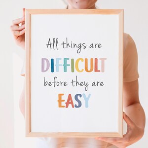 Puede incluir: Una impresión enmarcada con la cita "All things are DIFFICULT before they are EASY" en letras de colores. La cita es un mensaje motivacional sobre la perseverancia.