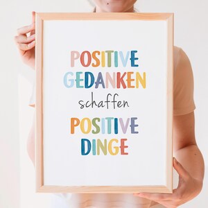 Peut inclure: Une impression encadr&eacute;e avec le texte "POSITIVE GEDANKEN schaffen POSITIVE DINGE" en lettres color&eacute;es. Le texte est en allemand et se traduit par "Les pens&eacute;es positives cr&eacute;ent des choses positives."