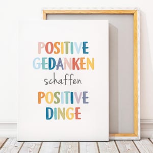 Peut inclure: Une impression sur toile blanche avec le texte "POSITIVE GEDANKEN schaffen POSITIVE DINGE" en lettres color&eacute;es. Le texte est en allemand et se traduit par "Les pens&eacute;es positives cr&eacute;ent des choses positives."