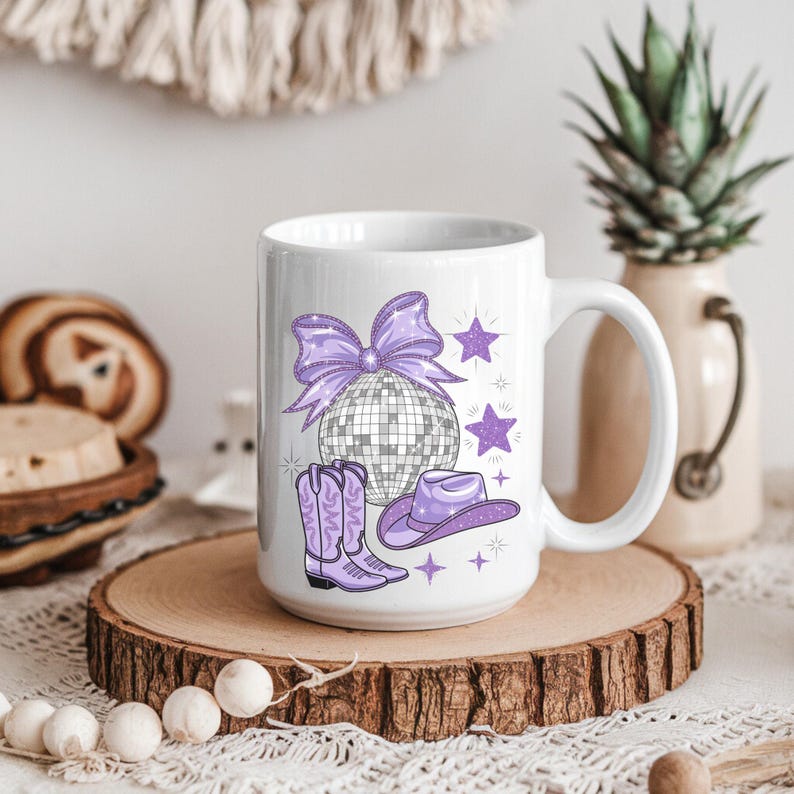 May include: White ceramic mug with a purple glitter design featuring a disco ball, cowboy hat, and boots. The design also includes a purple bow and stars.