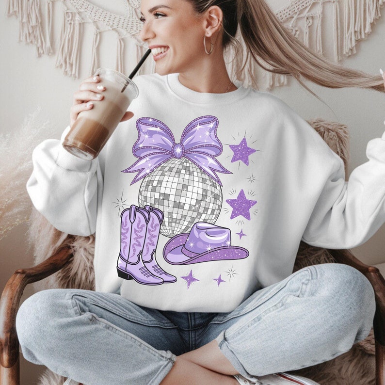 May include: White sweatshirt with a purple glitter bow, disco ball, cowboy hat, and boots. The design is centered on the front of the sweatshirt.