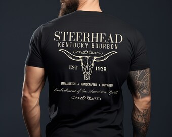 Op de afbeelding: Zwart T-shirt met een wit grafisch ontwerp met een stieren schedel en de tekst "STEERHEAD KENTUCKY BOURBON EST 1928 SMALL BATCH HANDCRAFTED DRY AGED Embodiment of the American Spirit"