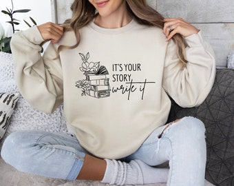 May include: A beige sweatshirt with a black graphic of a stack of books and flowers with the text "It's your story, write it".
