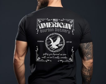 May include: Black t-shirt with a white graphic design of a vintage-style label for "American Bourbon Distillery" established "years ago". The label features an eagle inside a circle with the text "ORD" and the words "getting you liquored up since well...we can't really remember".