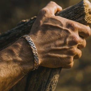 May include: A copper and silver cuff bracelet with a floral and rope design. The bracelet is worn on a person's wrist. The cuff is approximately 2 cm wide.