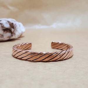 Adjustable copper cuff displayed on white background with faint shadow, highlighting shine and form.