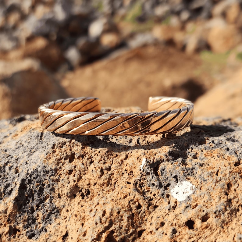 Twisted copper cuff bracelet resting on mossy stone in outdoor forest setting, highlighting earthy tones and texture