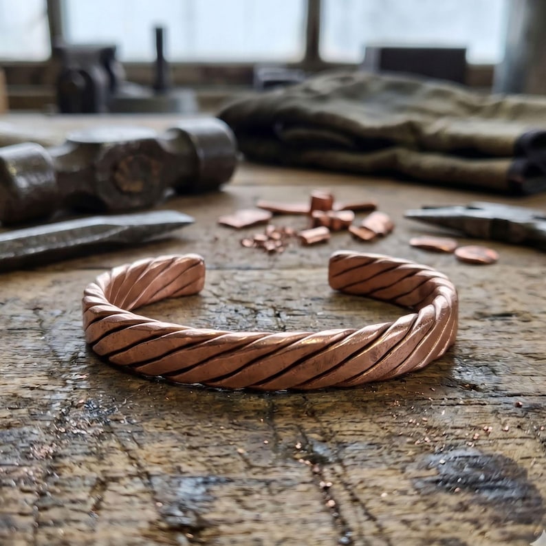 Copper bracelet resting on wooden jewelry workbench with tools, showcasing handmade craftsmanship and rustic style.