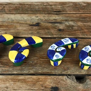 May include: A set of three ceramic mugs with a speckled, matte finish. The mugs are in shades of cream, light brown, and dark brown. Each mug has a simple, minimalist design and a rounded handle.