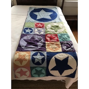 May include: A rectangular patchwork quilt featuring a variety of multi-colored fabric squares and rectangles, each decorated with a prominent star motif. The design includes shades of blue, green, red, orange, and purple, with stitched seams.
