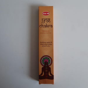 May include: A rectangular box of HEM Yog Chakra premium masala incense. The box is primarily brown with the brand name and product name in a stylized font. The box features an illustration of a person in a yoga pose and a mandala design.