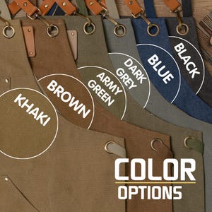 Op de afbeelding: Een close-up van een verscheidenheid aan canvas schorten in verschillende kleuren, waaronder kaki, bruin, legergroen, donkergrijs, blauw en zwart. De schorten hebben verstelbare banden en een grote zak aan de voorkant. De tekst "COLOR OPTIONS" wordt onder de schorten weergegeven.