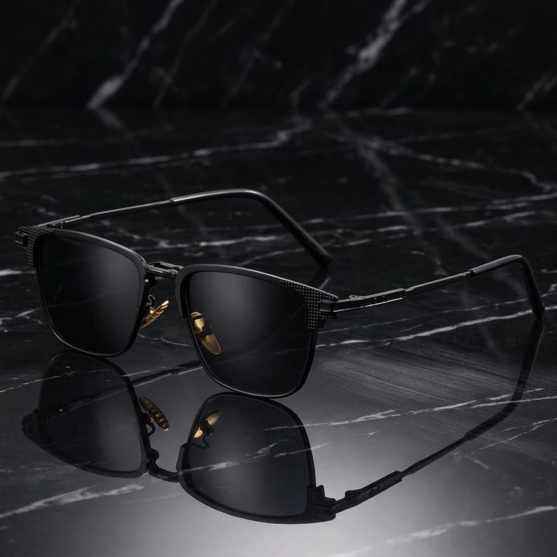 Puede incluir: Gafas de sol negras con montura rectangular y lentes oscuras. Las gafas de sol tienen un patr&oacute;n texturizado en las patillas y un dise&ntilde;o elegante y moderno. Las gafas se reflejan en una superficie oscura y brillante.