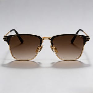 Puede incluir: Gafas de sol con montura dorada y detalles negros. Las lentes tienen un tinte degradado marr&oacute;n. Las gafas tienen una forma cuadrada cl&aacute;sica y un dise&ntilde;o moderno. Las patillas son negras y las almohadillas nasales doradas.