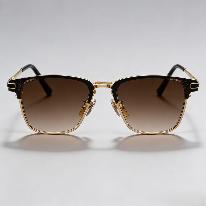 Puede incluir: Gafas de sol con montura dorada y detalles negros. Las lentes tienen un tinte degradado marr&oacute;n. Las gafas tienen una forma cuadrada cl&aacute;sica y un dise&ntilde;o moderno. Las patillas son negras y las almohadillas nasales doradas.