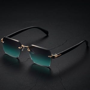 May include: Rimless sunglasses with a gradient teal and black lens. The frames are gold-colored, and the arms are black. The sunglasses are set against a dark background.