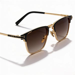 Puede incluir: Gafas de sol con montura dorada, detalles negros y lentes degradadas marrones. El dise&ntilde;o presenta una forma cl&aacute;sica con una est&eacute;tica moderna. Las lentes van de oscuro a claro. La montura es dorada y las patillas son negras.