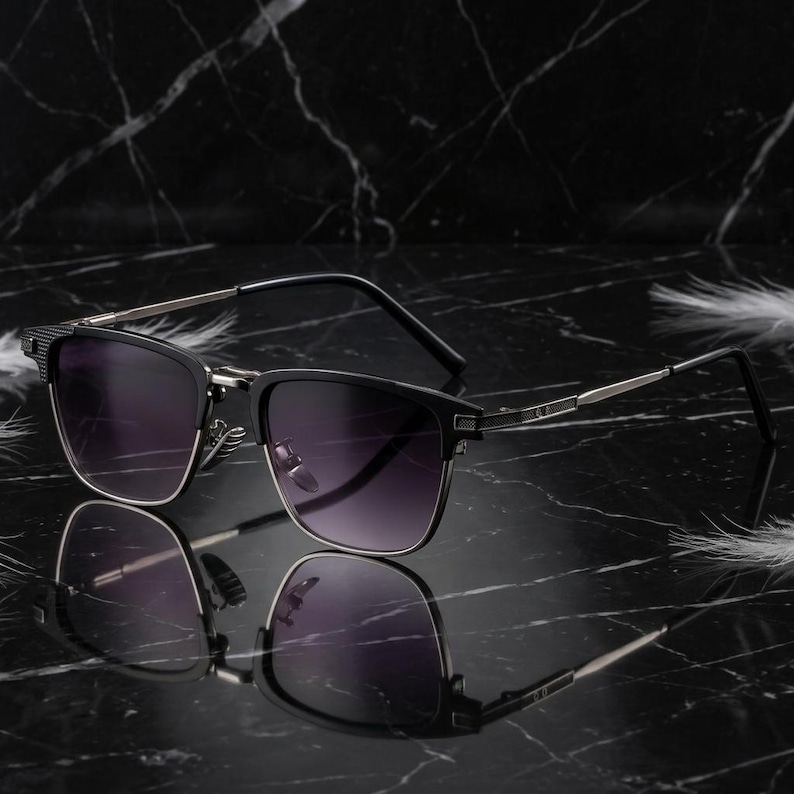 Puede incluir: Gafas de sol negras con montura cuadrada y lentes degradadas. Las gafas tienen patillas plateadas y detalles texturizados en las sienes. Las lentes hacen una transici&oacute;n de oscuro a claro.