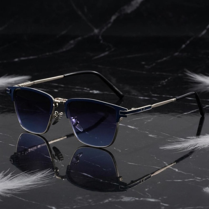 Puede incluir: Gafas de sol azules y plateadas con lentes degradadas. La montura rectangular tiene un puente y varillas plateadas. Las lentes pasan de azul oscuro a azul claro. Reflejo sobre una superficie oscura.