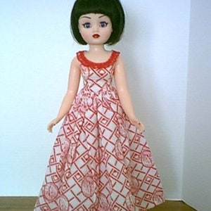 May include: A doll with black hair and blue eyes wearing a white dress with red and white geometric patterns.