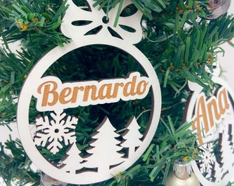 May include: White wooden Christmas ornament with a snowflake and pine tree design. The ornament has the name "Bernardo" written in brown letters.