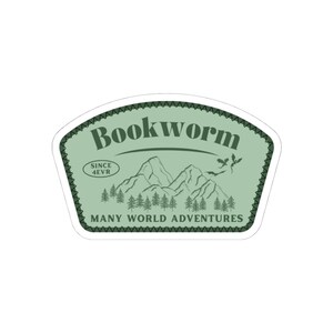 Peut inclure: Un autocollant vert avec le mot "Bookworm" dans une police stylisée. L'autocollant représente une chaîne de montagnes, des arbres et le texte "SINCE 4EVR" et "MANY WORLD ADVENTURES". L'autocollant a une bordure festonnée.