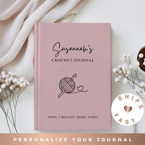 May include: A dusty rose hardcover journal with black text that reads Susannah's CROCHET JOURNAL and OOPS, I BOUGHT MORE YARN! A black line drawing of a ball of yarn with a crochet hook and a small heart is centered on the front cover.