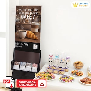 May include: A black display stand with the text "Est-ce mal de faire une pause CAFE?" and "BOIS TON CAFÉ BIEN CHAUD". The stand features a coffee and pastry image. Various treats and packaged goods are on a white table.