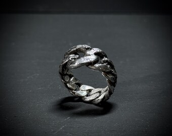 May include: A silver ring with a chunky chain design. The ring is made of metal and has a textured surface.