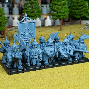 May include: A collection of blue miniature figurines, likely for a tabletop game. The figures are clad in detailed armour and helmets, some wielding axes, swords, and a banner. They are positioned on a black base, against a green and brown background.