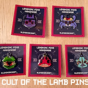 Puede incluir: Cinco pines de esmalte con personajes del videojuego "Cult of the Lamb". Los pines son en blanco y negro con acentos rojos y presentan una variedad de personajes, incluyendo un cangrejo, una criatura con múltiples ojos, una criatura con cabeza verde, una criatura con cabeza roja y una criatura con cabeza azul. Los pines están todos etiquetados con "LEMONIAC PINS HANDMADE" y "@LEMONIACRAFT_"