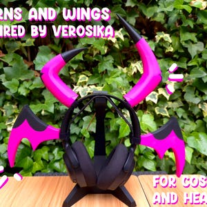 Puede incluir: Cuernos y alas rosas y negras para cosplay y auriculares. Los cuernos y las alas están unidos a un soporte de auriculares negro. El texto "HORNS AND WINGS INSPIRED BY VEROSIKA" está en la parte superior de la imagen. El texto "FOR COSPLAY AND HEADSET" está en la parte inferior de la imagen.