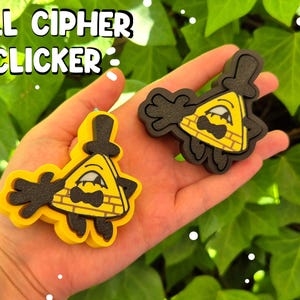 May include: Two yellow and black Bill Cipher Clicker charms. The charms are shaped like a yellow triangle with a black top hat, bow tie, and arms. The text "BILL CIPHER CLICKER" is above the charms.