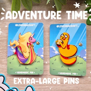 Può includere: Due spille smaltate con personaggi di Adventure Time su sfondo blu. Le spille sono extra large e raffigurano Finn l'Umano e la Principessa Bubblegum. Le spille sono fatte a mano e hanno uno sfondo bianco con il testo "Handmade Pin" in basso.
