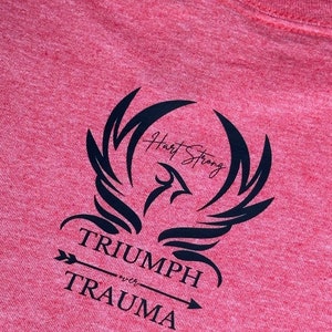 May include: Red t-shirt with a black graphic of a phoenix with the text "Heart Strong" and "Triumph over Trauma" with an arrow pointing to the right.