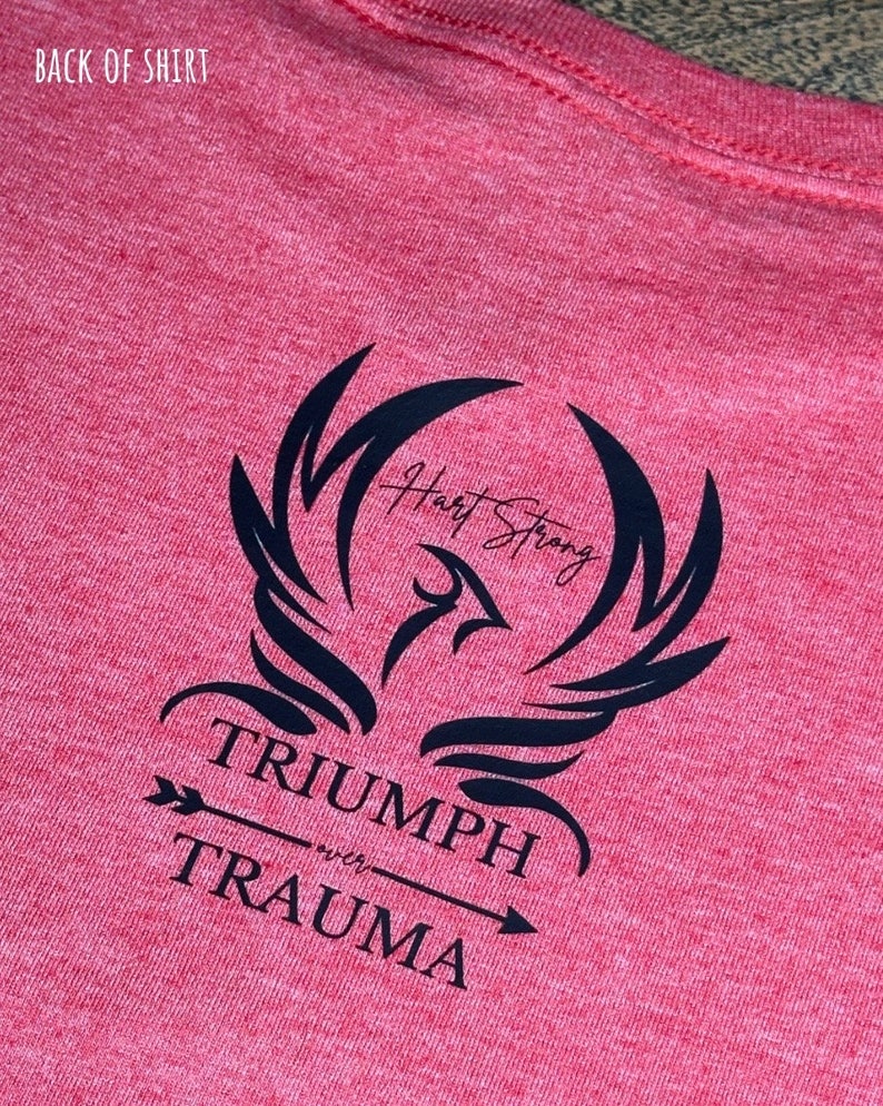 May include: Red t-shirt with a black graphic of a phoenix with the text "Heart Strong" and "Triumph over Trauma" with an arrow pointing to the right.