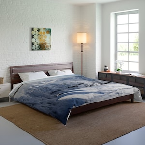 May include: A blue and white duvet cover with a geometric pattern. The duvet cover is on a bed with a wooden frame and white pillows. The bed is in a bedroom with a white brick wall, a window, and a lamp.