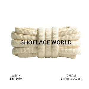 Peut inclure: Lacets de couleur crème, enroulés serrés, avec le texte "SHOELACE WORLD" imprimé au centre. La largeur est de 8,5 à 9 mm. L'image montre une paire de lacets.