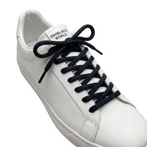 May include: White leather sneaker with black shoelaces. The shoelaces are tied in a bow. The text "SHOELACE WORLD" is printed on the tongue of the shoe.