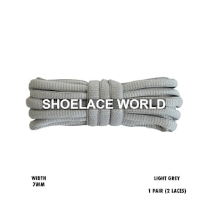 May include: Light grey shoelaces, 7mm wide, in a neatly coiled bundle. The text "SHOELACE WORLD" is printed across the laces. The product description also includes "LIGHT GREY" and "1 PAIR (2 LACES)".