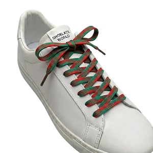 Puede incluir: Zapatilla de cuero blanco con cordones a rayas rojas y verdes, atados con un lazo. El texto "SHOELACE WORLD" es visible en la lengüeta del zapato.