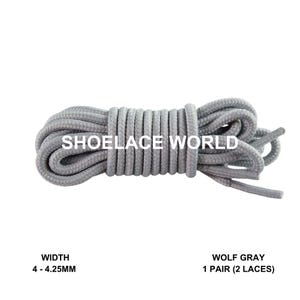 Op de afbeelding: Een bundel wolfgrijze veters. De veters zijn lichtgrijs van kleur en zijn opgerold. De tekst "SHOELACE WORLD" staat op de veters. De breedte is 4 - 4,25 mm. Eén paar (2 veters) is inbegrepen.