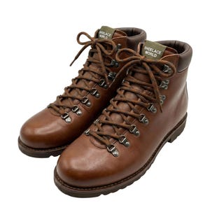 Op de afbeelding: Een paar bruine leren wandelschoenen met donkerbruine gevoerde kragen en bruine veters. De schoenen zijn voorzien van metalen D-ring oogjes en een groen label op de tong met de witte tekst SHOELACE WORLD. De zolen zijn donkerbruin met profiel.