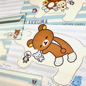 May include: A light blue and white striped background with a brown bear wearing a blue and white striped scarf and blue and white striped socks. The bear is holding a small blue and white bear. The text "Rilakkuma" is written in black on a white background. The text "Tomorrow is another stripes" is written in black on a white background.